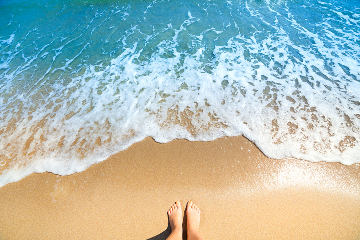 Sea foam, waves and naked feet on a sand beach