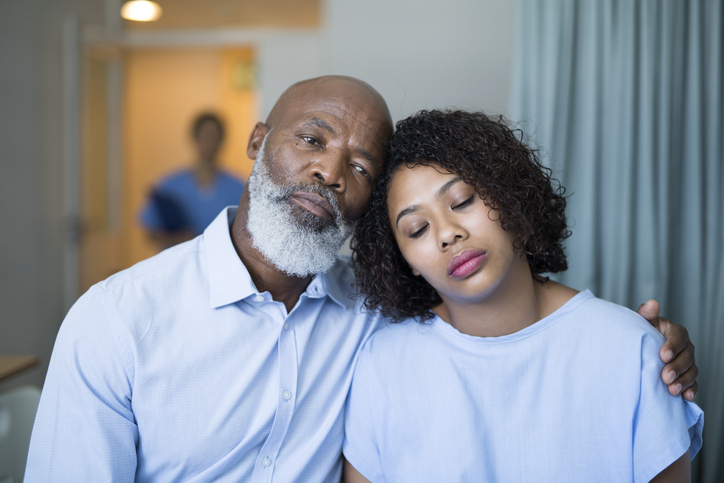 Sad mature man consoling young patient. Father is embracing while sitting with sick daughter. They are on hospital bed at ward.